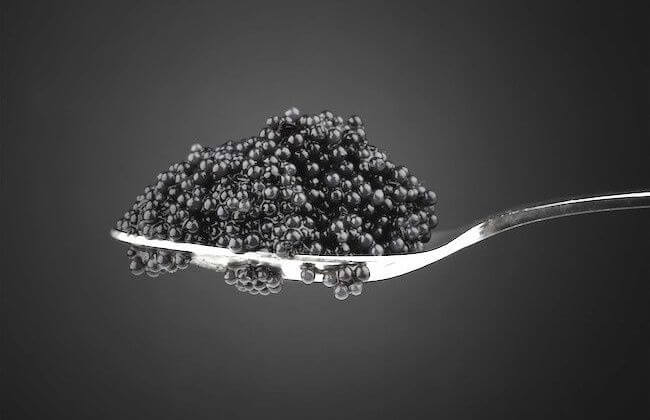 Black caviar in metal teaspoon. Macro photo on dark background