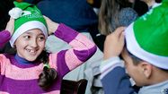 Deux enfants souriant avec des bonnets de Noël aux couleurs du Secours Populaire.