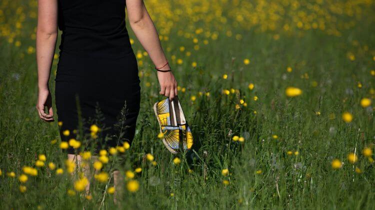 Une femme dans un champs tiens une paire d'espadrilles Zétoiles jaunes et bleues.
