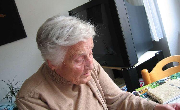 Une vieille dame assise à une table dans son domicile.