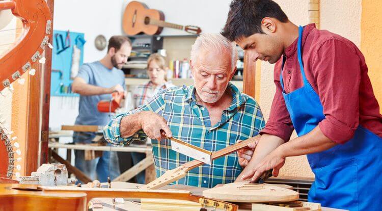 Un jeune homme montre à un homme plus âgé comment fabriquer un manche de guitare.