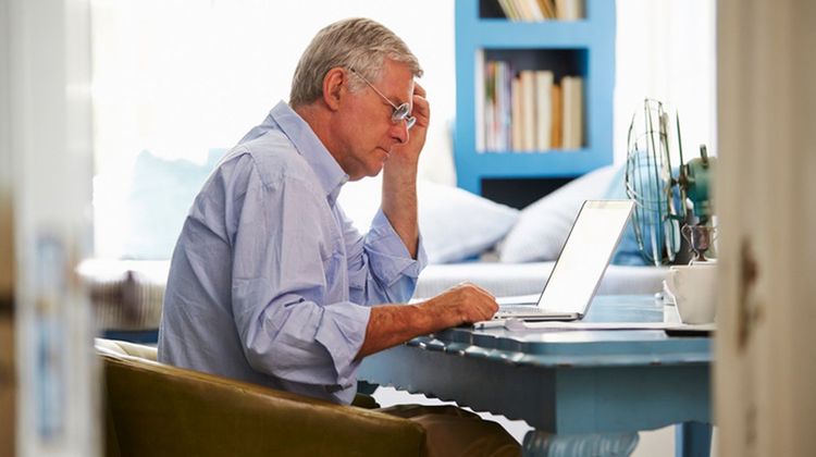 Un homme âgée pensif devant son ordinateur.