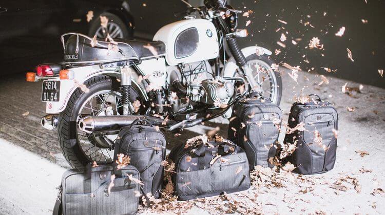 Plusieurs sacs de la gamme MUB exposés devant une moto dans un parking.