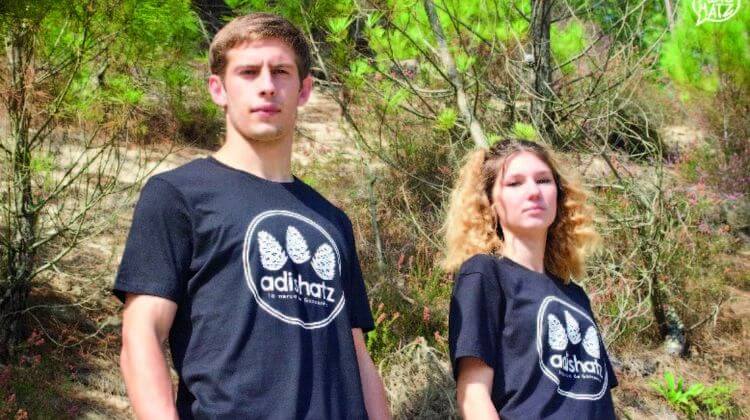 Un jeune homme et une jeune femme, dans la forêt landaise avec des t-shirts Adishatz.
