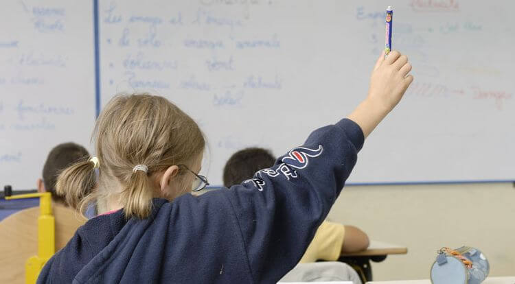 Une jeune fille lève la main en classe.