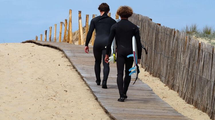 Deux surfeurs marchent dans le sable pour rejoindre la plage.