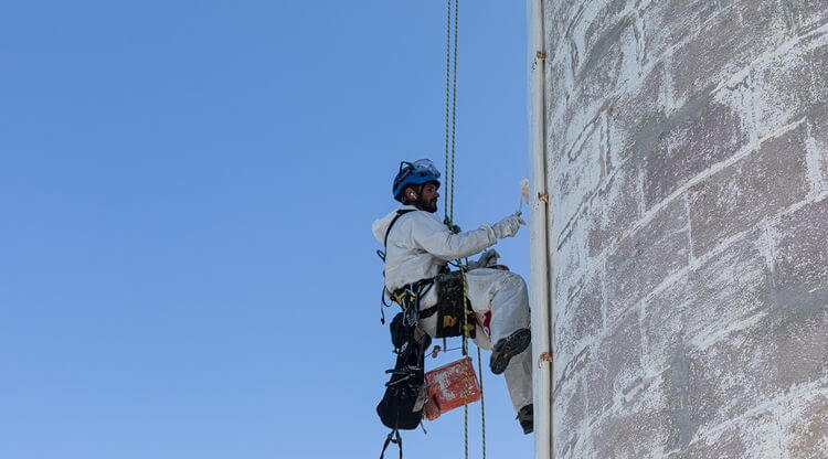 Un employé de ATS travaille sur le phare de Biarritz, attaché à des cordes.