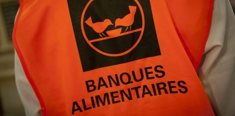 Un bénévole de la Banque Alimentaire porte le gilet orange de l'association avec le logo.