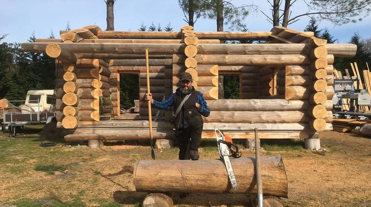 Simon Claisse pose devant sa maison en rondins de bois dans les Landes.