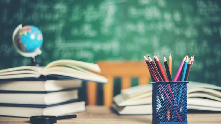 Un pot de crayons de couleurs et un tas de livres sur un bureau de maitresse d'école