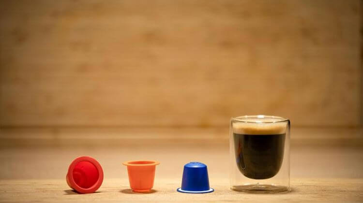 Une tasse de café posée sur une table et ses 3 capsules en exposition