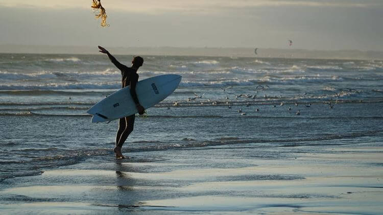 Un surfeur tiens sa planche sous le bras sur la plage.