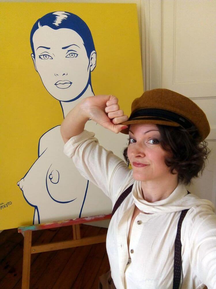 Virginie Poeyto devant un de ses tableaux de femmes seins nus tenant son chapeau