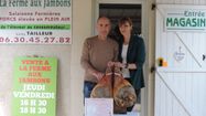 Daniel Tailleur pose avec deux de ses jambons, dans sa ferme dans le Béarn.