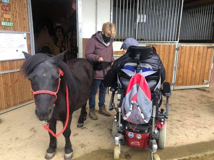 Une personne en situation de handicap s'occupe d'un poney, avec l'aide d'une personne valide.