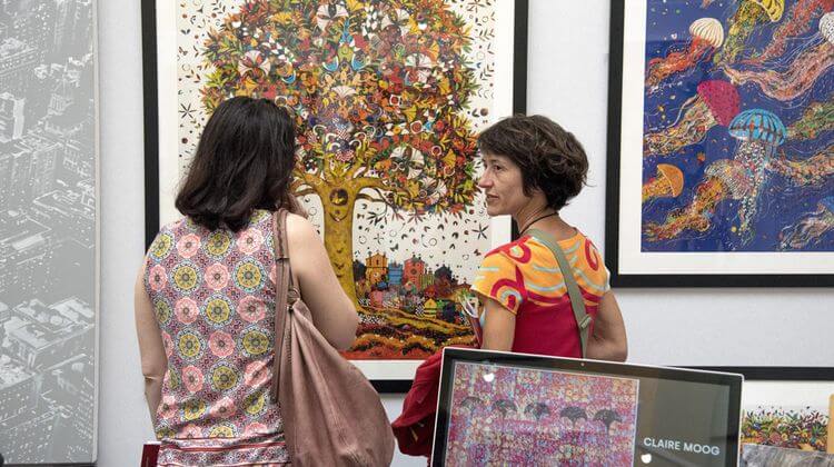 Deux visiteuses discutant face à des tableaux exposés