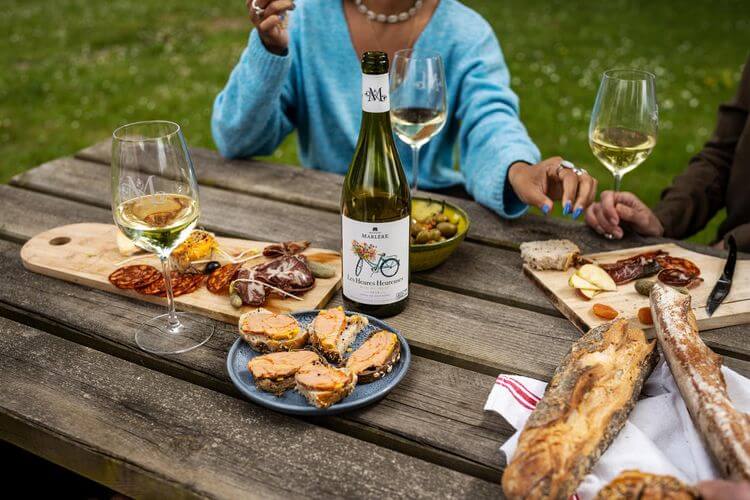 Photo d'un pique-nique entre amis sur une table en bois avec une bamis avec une bouteille de vin et  amuse-bouche