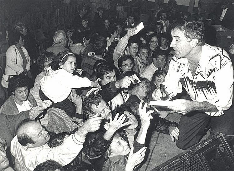 Le chanteur Michel Etcheverry au bout d'une scène accroupi signant des autographes à une foule de fans