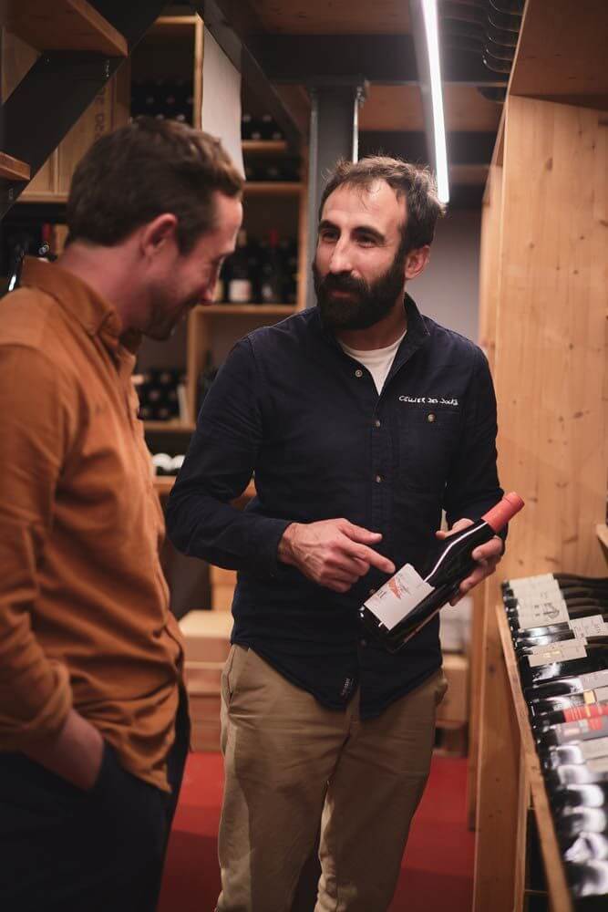 Julien Combes : premier maître caviste du Pays basque dans sa boutique proposant une bouteille de vin à un client