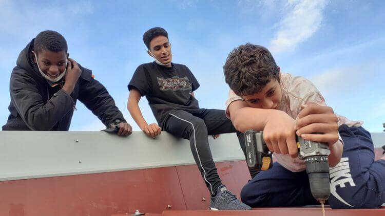 un groupe de 3 jeunes sur un toit dont un qui revisse une tolle