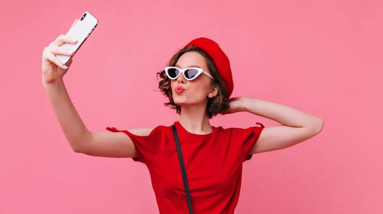 Une dame se prend en selfie. Elle porte des lunette de soleil blanche, une robe rouge et un chapeau rouge.