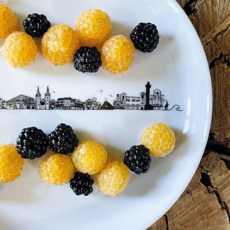 Une assiette de la créatrice est posée sur une table. Dans l'assiette, on y retrouve des framboises noires et jaunes.