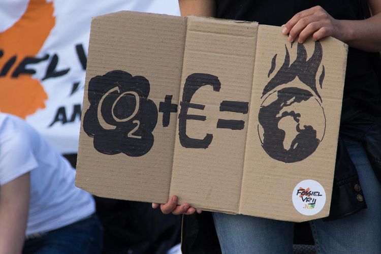 Dessin sur une pancarte où il est indiqué : CO2 + euros = planète qui brûle