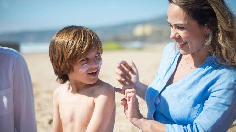 Une mère étale de la crème solaire sur son fils à la plage.