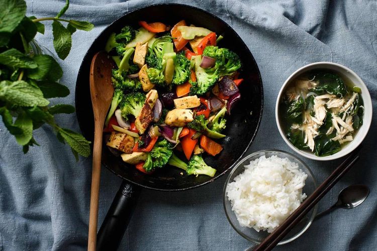 Poelé de légumes au poulet servis dans une poêle avec un bol de riz blanc et une soupe chinoise poulet épinards
