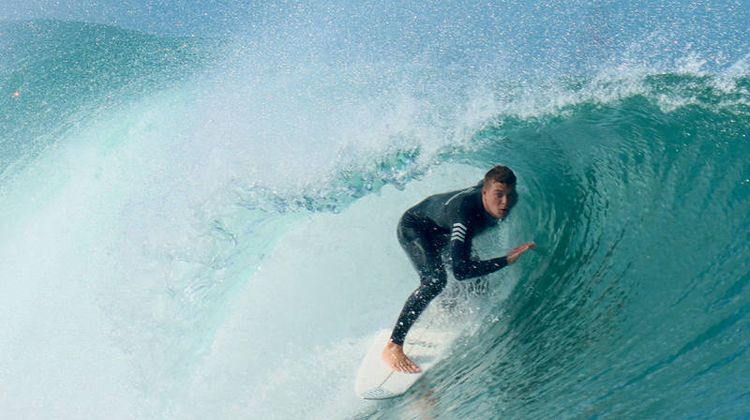 Un surfeur dans une vague avec une combinaison Wetty.
