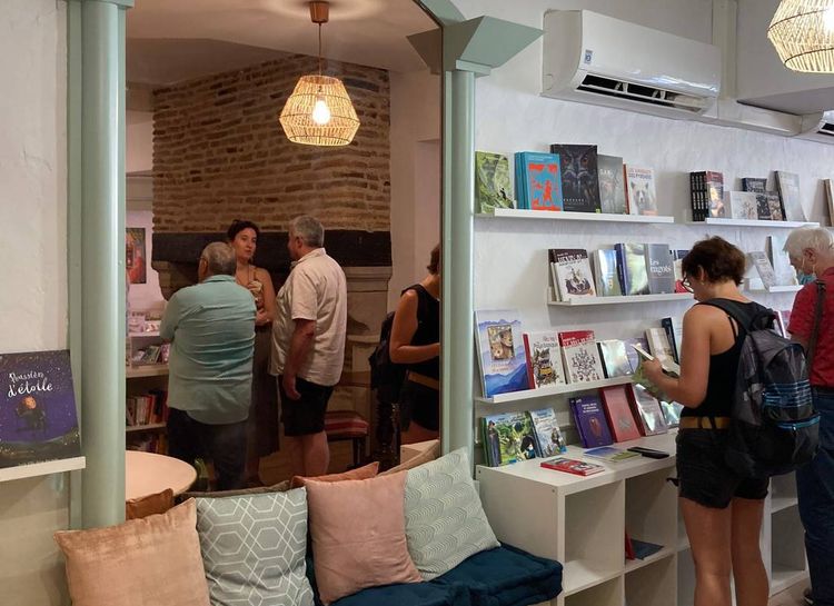 Des clients de Danser sous la plume à Pau observent des livres dans la librairie au premier plan, et consomment des gourmandises dans le salon de thé au second plan.