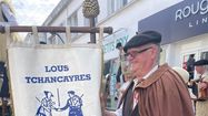 Bernard Escaffre pose avec la bannière de Lous Tchancayres, association pour laquelle il fabrique des échasses.