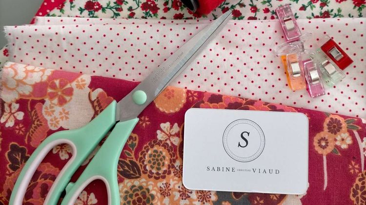 Un ciseau, du tissu et la carte de visite de Sabine Viaud, créatrice de sac à main et d'écharpes, à Mourenx.