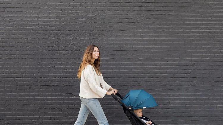 Une femme promène un bébé dans une poussette dans la rue.