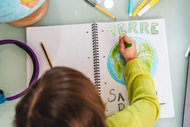 Une enfant dessine la planète sur un cahier.