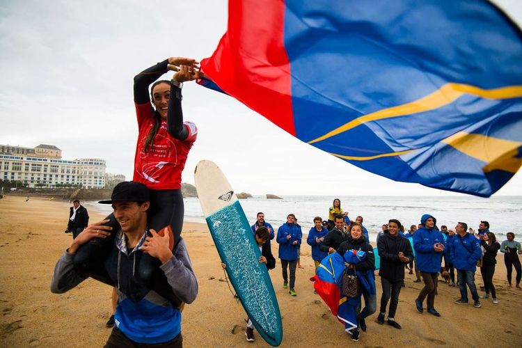 Une surfeuse célèbre une victoire avec un drapeau sur le dos de son manager.