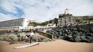 Un surfeur se prépare sur l'une des plages de Biarritz avec la ville et le public derrière lui.