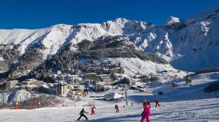 Des skieurs descende une piste avec en fond les Pyrénées et la station de Gourette.