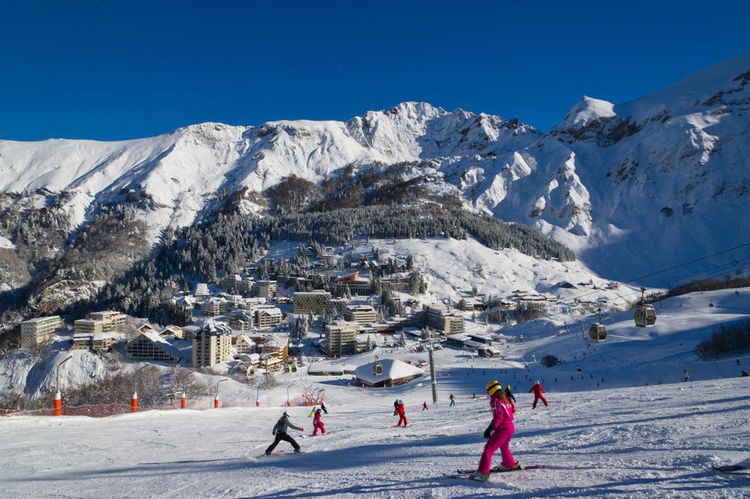 Des skieurs descende une piste avec en fond les Pyrénées et la station de Gourette.