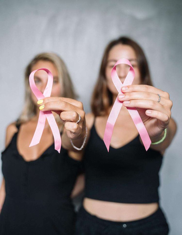 Deux jeunes femmes tiennent dans leur main le symbole de la lutte contre le cancer du sein.