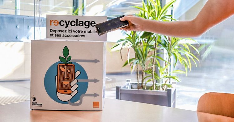 Une femme met son téléphone mobile obsolète dans une caisse de récolte d'Orange afin qu'il soit recyclé et réutilisé.