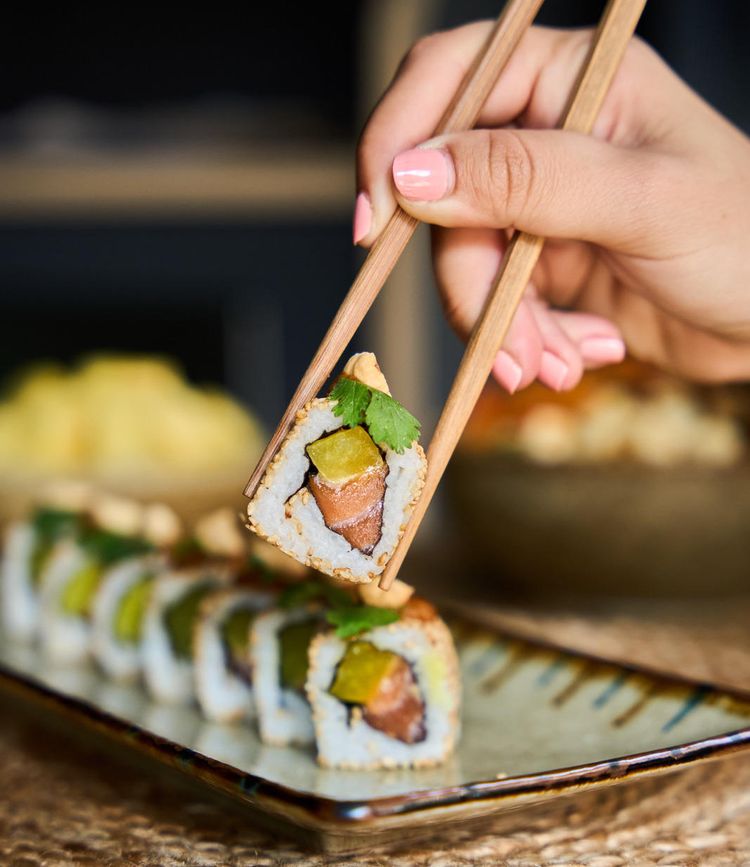 Une femme prends un sushi avec des baguettes.