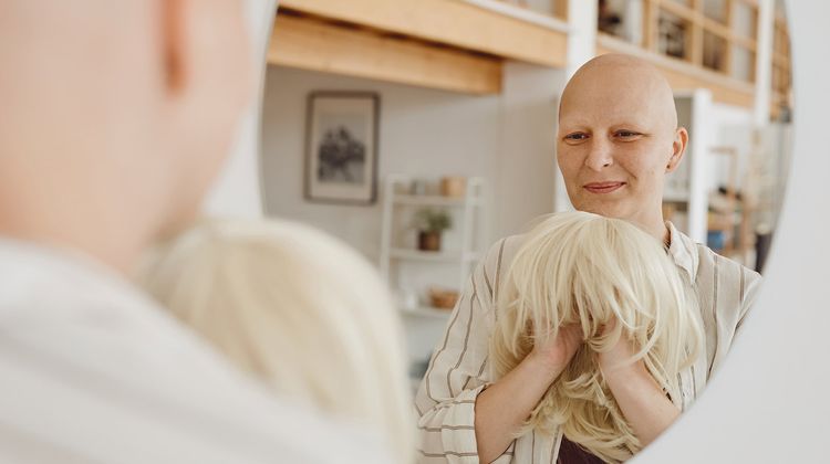 Photo d'une femme malade se regardant dans un miroir avec une perruque à la main