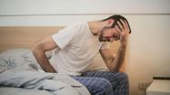 Un homme s'assoit sur son lit en ayant mal à la tête.