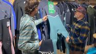 Deux personnes regardent des combinaisons de surf dans une boutique.