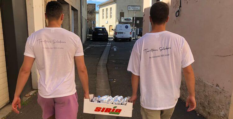 Deux membres de l'association Territoire Solidaire portent une cagette pleine de bouteilles d'eau.