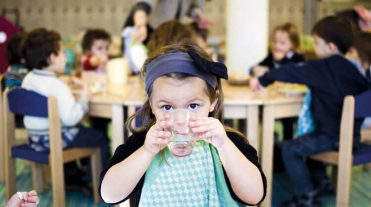 Une petite fille boit dans un verre d'eau dans une cantine scolaire.