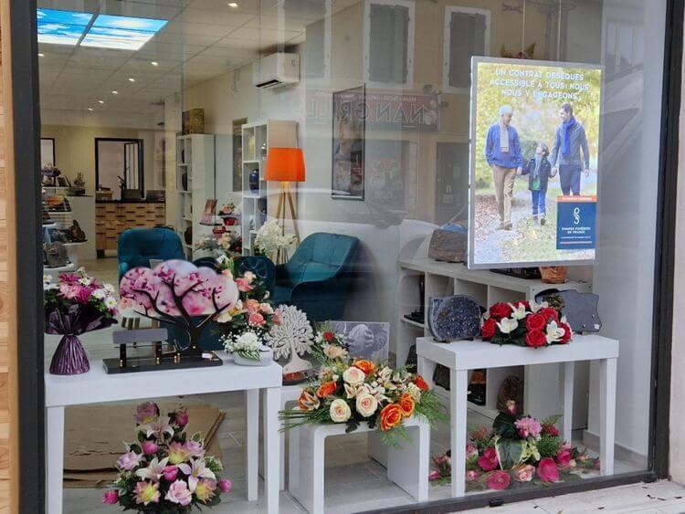 la vitrine du magasin de Camille Berot avec des fleurs, des plaques mortuaires et une vue sur l'intérieur avec des fauteuils pour accueillir les familles