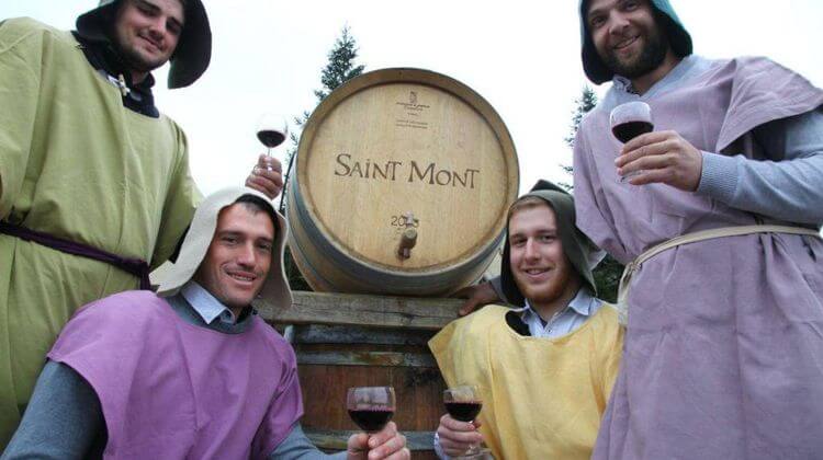 Quatre vignerons habillés comme au Moyen âge tenant un verre de vin rouge devant un tonneau Saint Mont