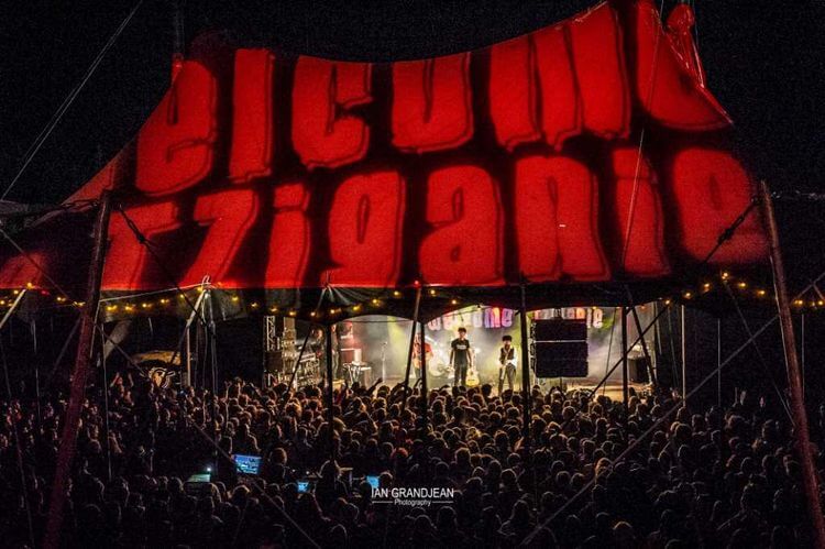 Une vue du chapiteau la nuit avec Welcome in Tziganie en grosses lettres rouges et la foule tournée vers la scène
